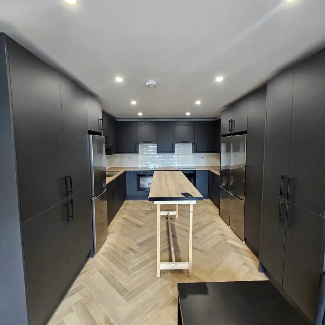 Modern galley kitchen with dark cabinets, island, and herringbone floor.