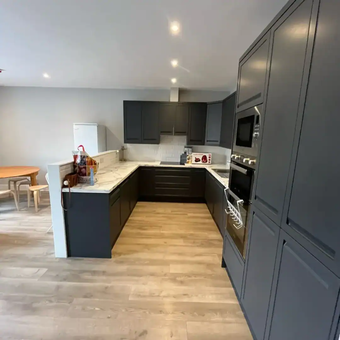 Modern kitchen with dark gray cabinets, marble countertops, and light wood flooring.