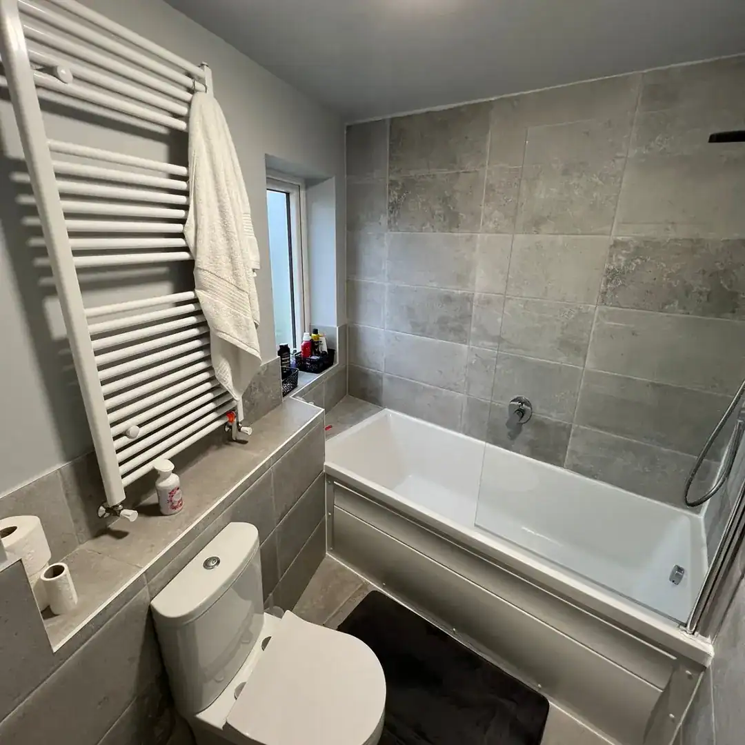 Modern bathroom with gray tile, white tub, toilet, and towel warmer.