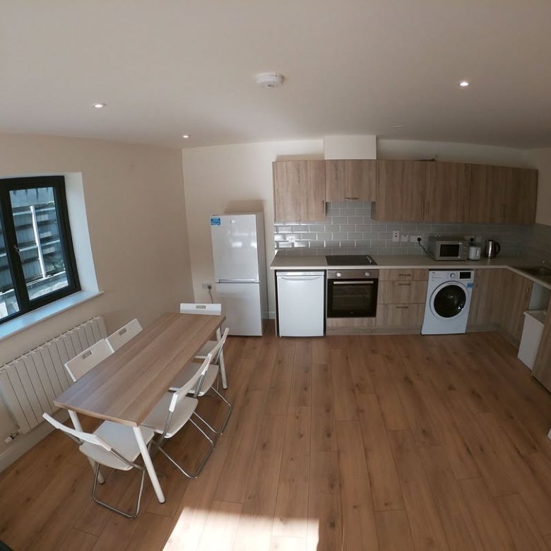Open-plan kitchen and dining area with wooden floor, white appliances, and window with black frame.