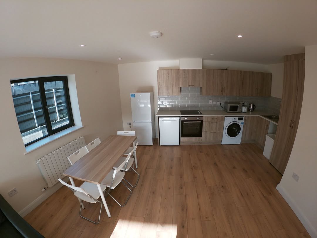 Open-plan kitchen and dining area with wooden floor, white appliances, and window with black frame.