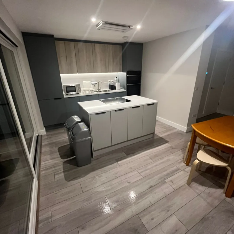 Modern kitchen with island, gray cabinets, wood floors, and dining table.