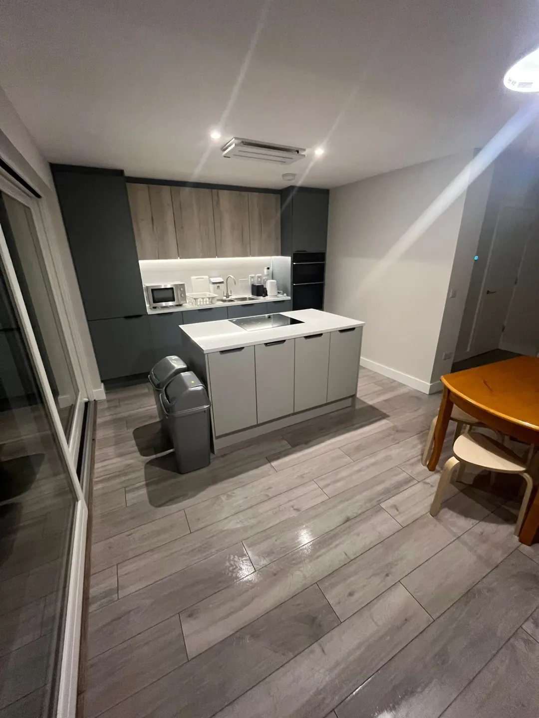 Modern kitchen with island, gray cabinets, wood floors, and dining table.