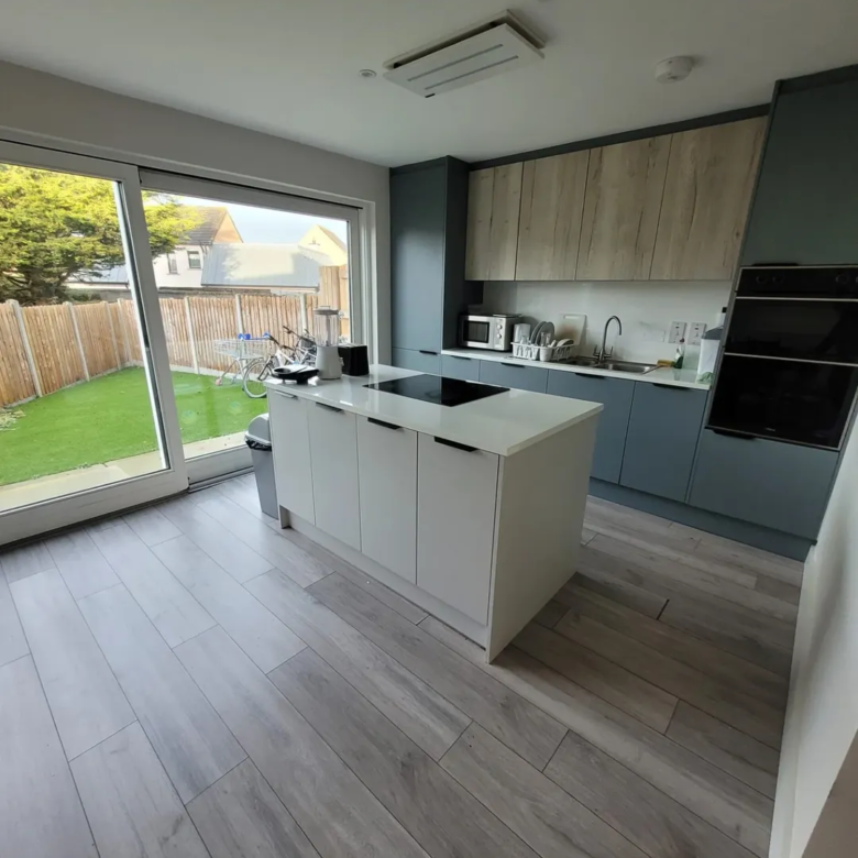 Modern kitchen with island, grey cabinets, wood accents, and garden view.