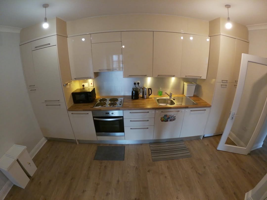 Modern kitchen with light wood cabinets, steel backsplash, and wood-look flooring.