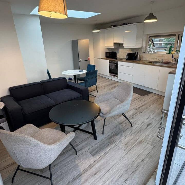 Modern kitchen and living area with sofa, chairs, table, and white cabinets.