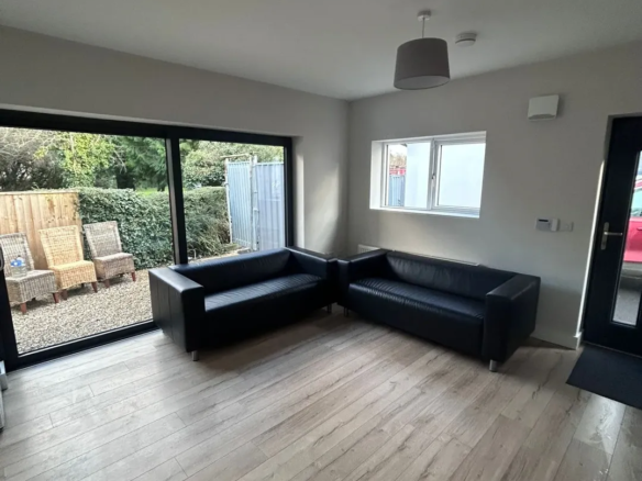 Modern living room with black sofas, wood floors, and sliding glass doors to a garden.
