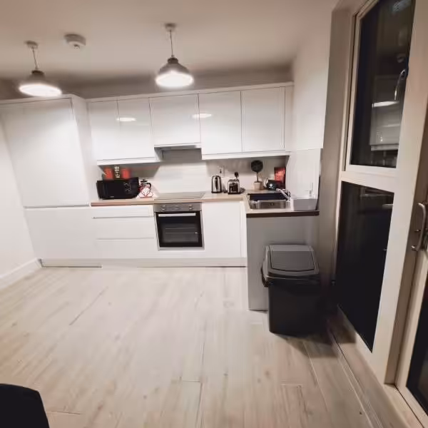 Modern white kitchen with wood-look floors, stainless steel appliances, and bright lighting.