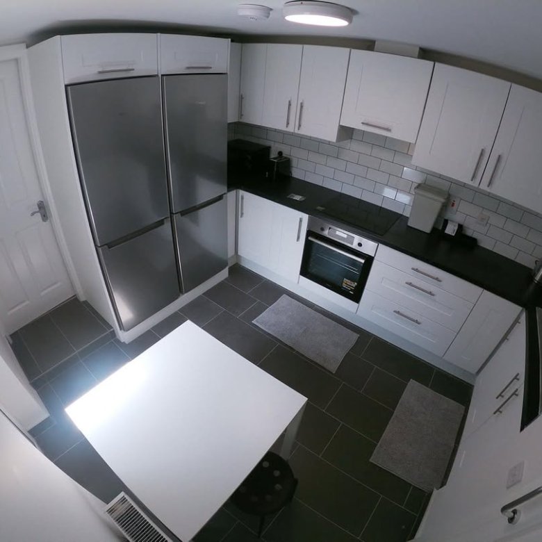 Modern white kitchen with stainless steel refrigerator, black countertops, and a white table.