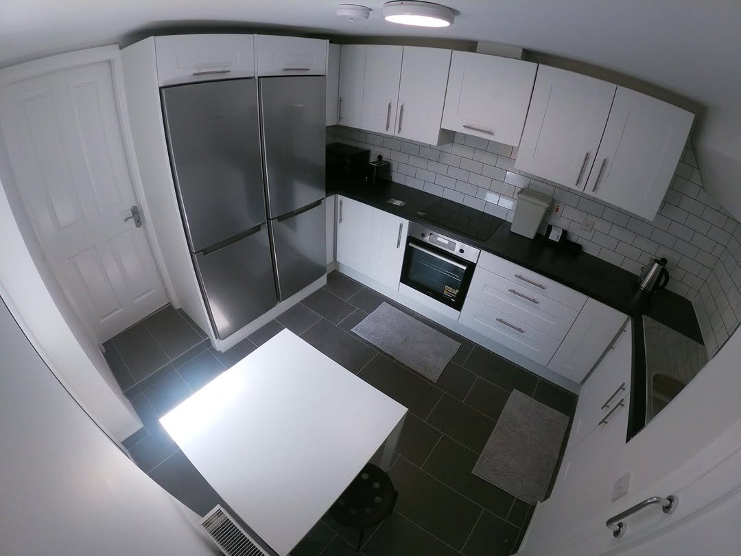 Modern white kitchen with stainless steel refrigerator, black countertops, and a white table.