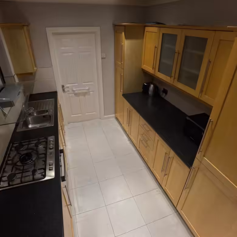 Narrow kitchen with light wood cabinets, black countertops, gas hob, and white door.