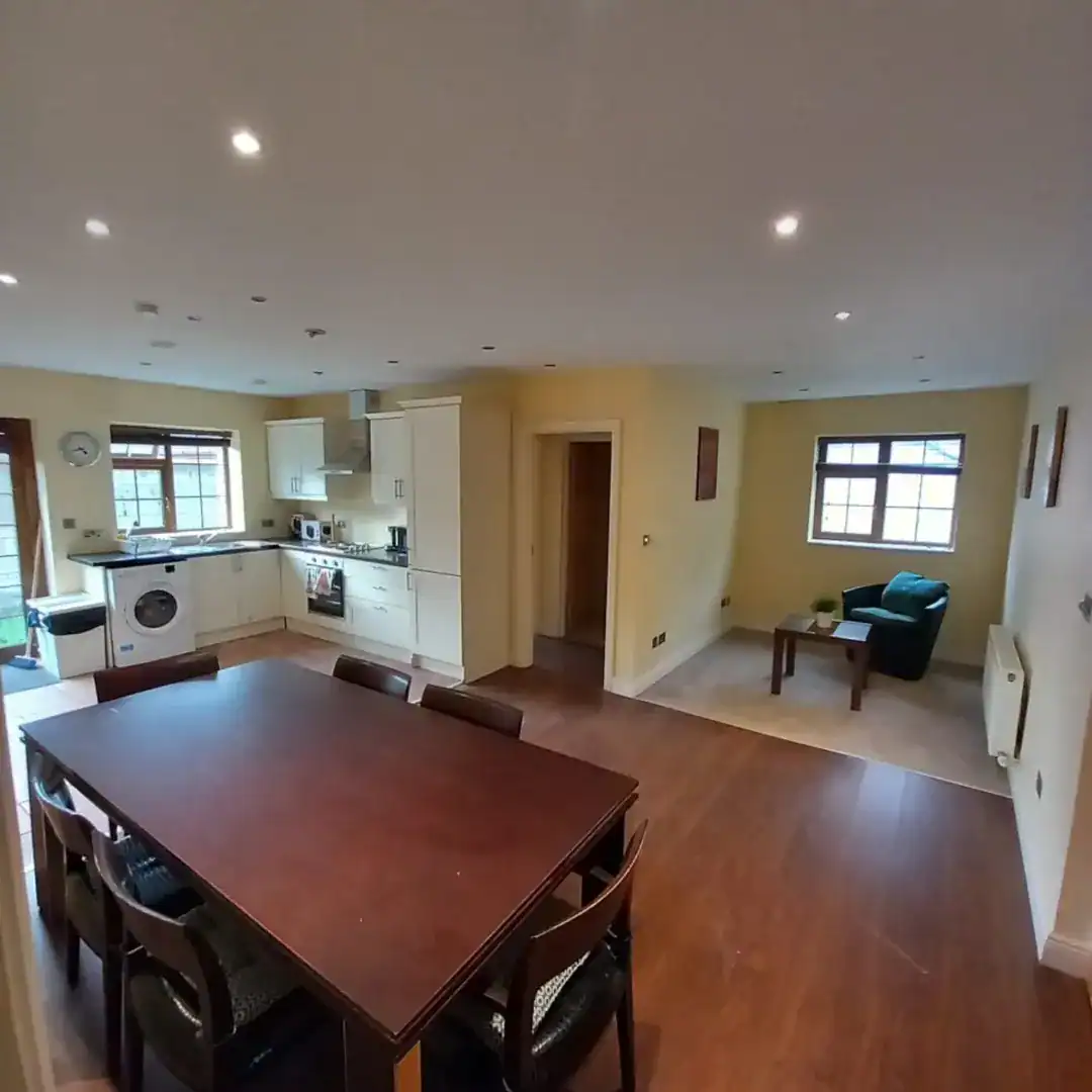 Open-plan kitchen and dining area with wood floors, table, and armchair.