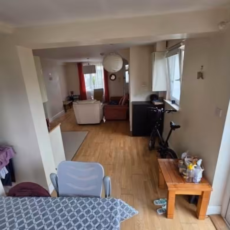 Open-plan living space with seating, bike, table, and view into a living room with red curtains.