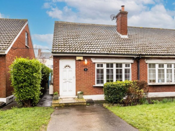 Red brick bungalow with white door and windows, green bushes, and a chimney.