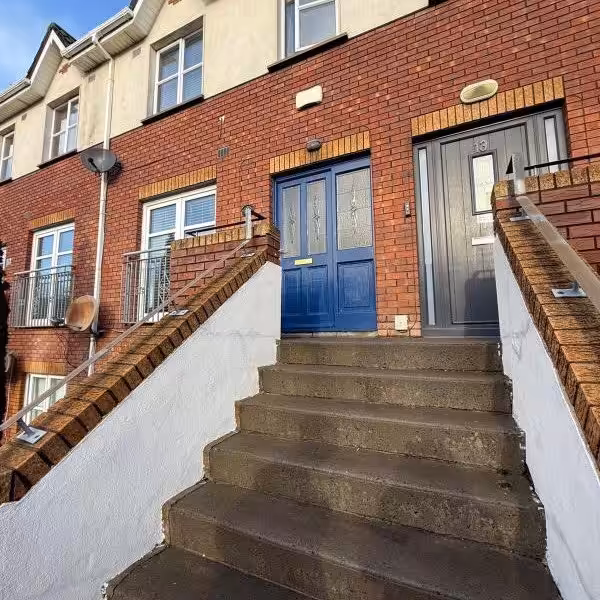 Red brick townhouse with blue door and concrete steps leading to the entrance.