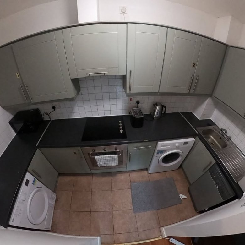 Small kitchen with sage green cabinets, black countertops, appliances, and tile backsplash.