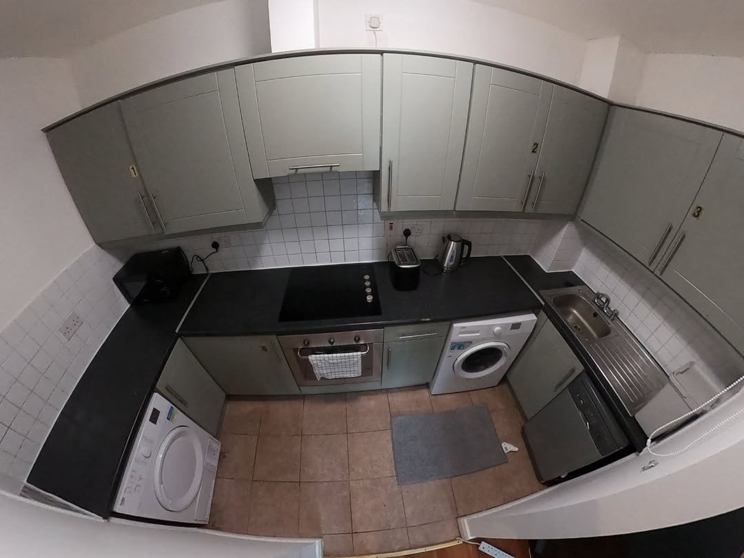 Small kitchen with sage green cabinets, black countertops, appliances, and tile backsplash.