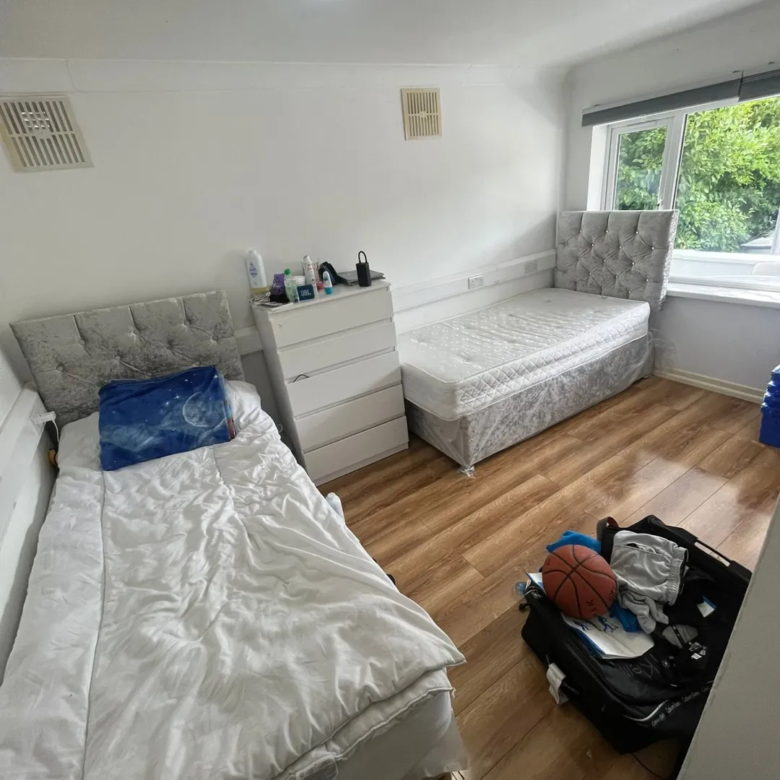 Shared bedroom with two beds, dresser, wood floor, and window with natural light.