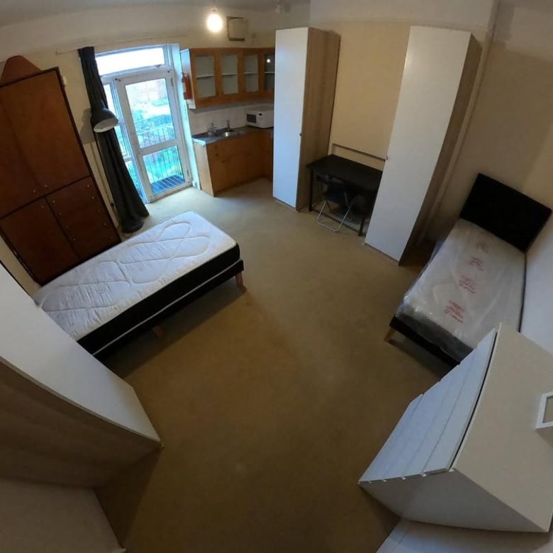 Small apartment room with beds, kitchenette, desk, and storage units.