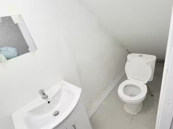 Small white bathroom with toilet, sink, and mirror in an attic space.