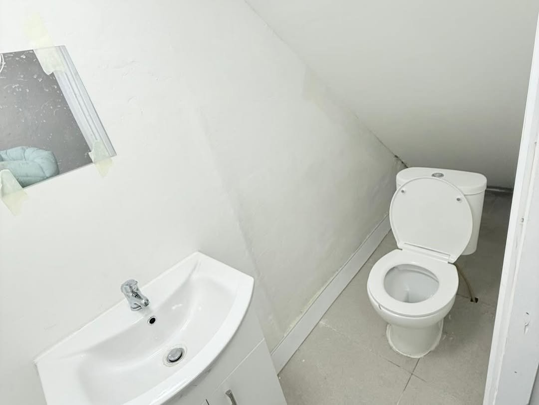 Small white bathroom with toilet, sink, and mirror in an attic space.