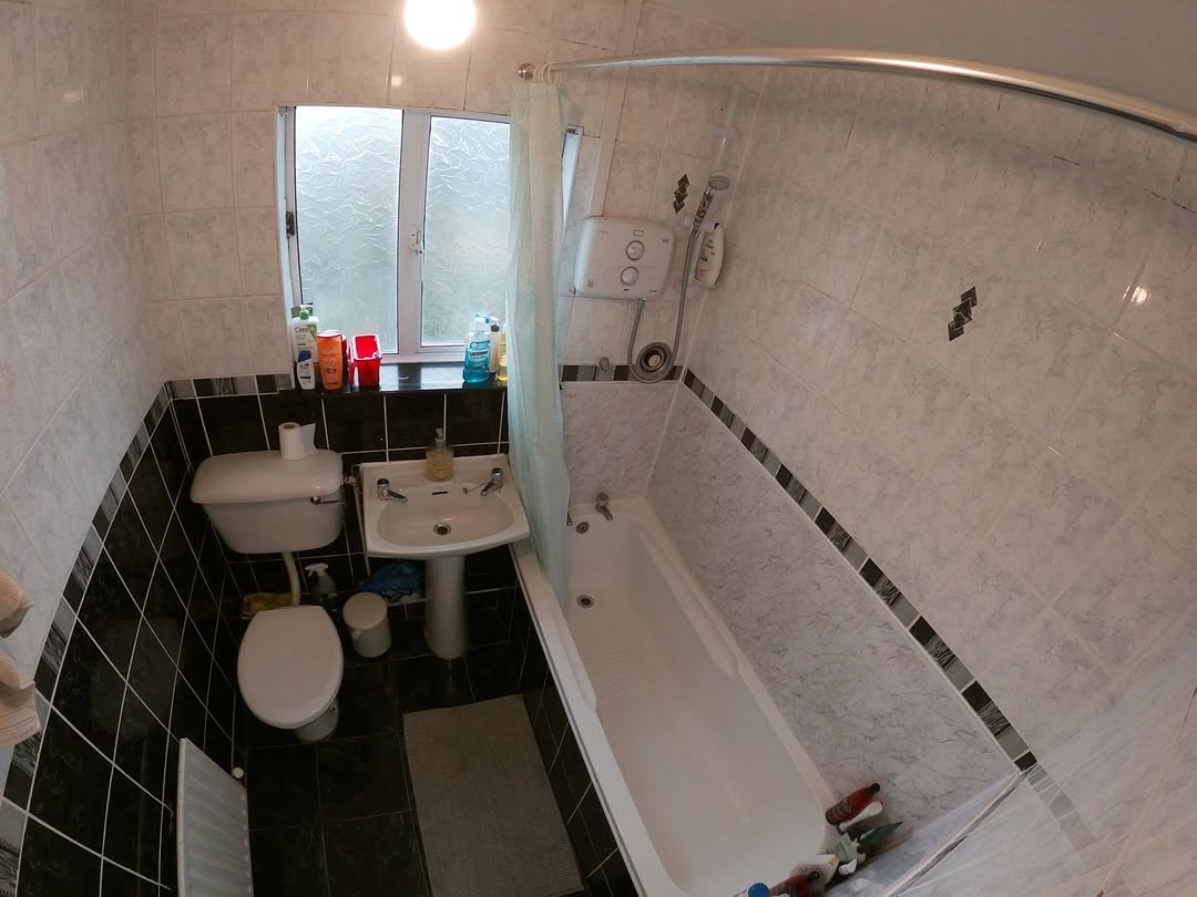 Small bathroom with black and white tiles, bathtub, toilet, and sink under a window.