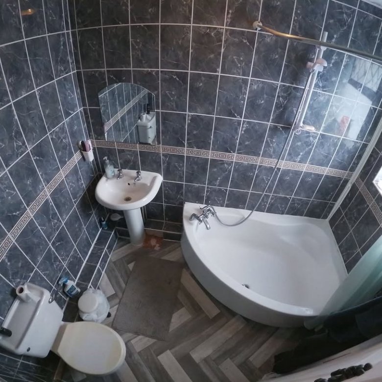 Small bathroom with gray tiles, pedestal sink, toilet, and corner bathtub with shower.