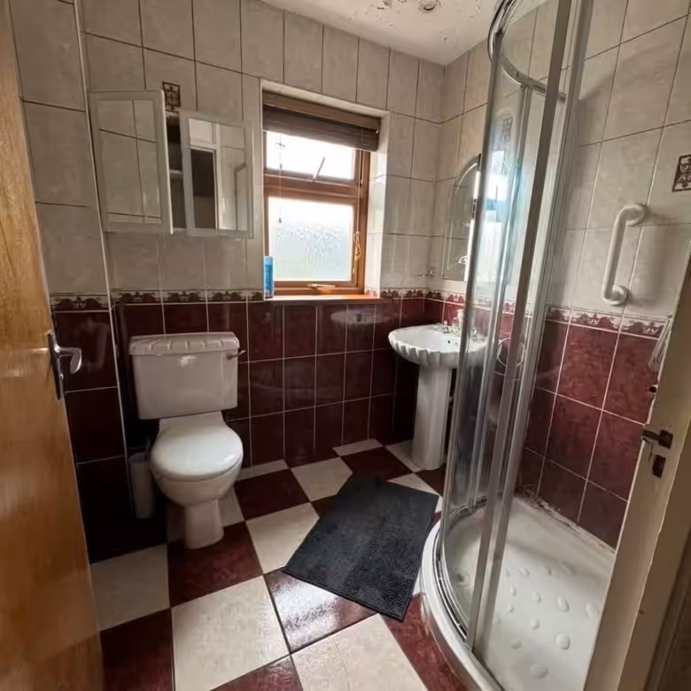 Small bathroom with red and cream tiles, toilet, sink, and shower.
