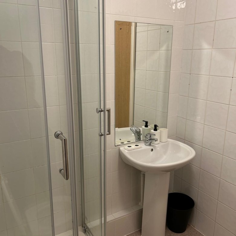 Small bathroom with shower, pedestal sink, and mirror in a tiled room.