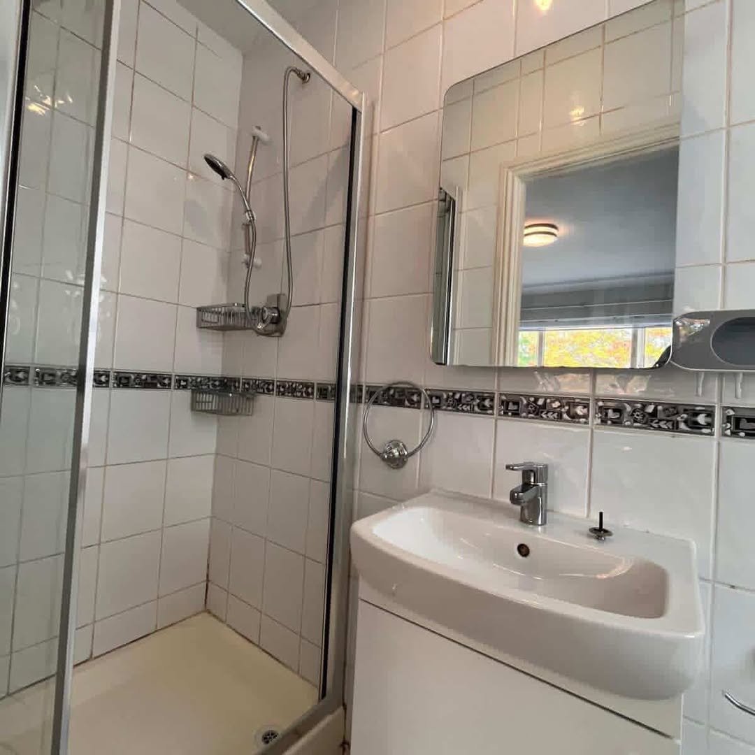 Small bathroom with shower, sink, and mirror. White tile with decorative border.
