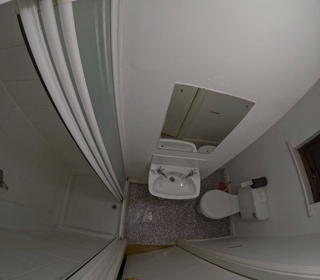 Small bathroom with shower, sink, toilet, and mirror. Tiled floor.