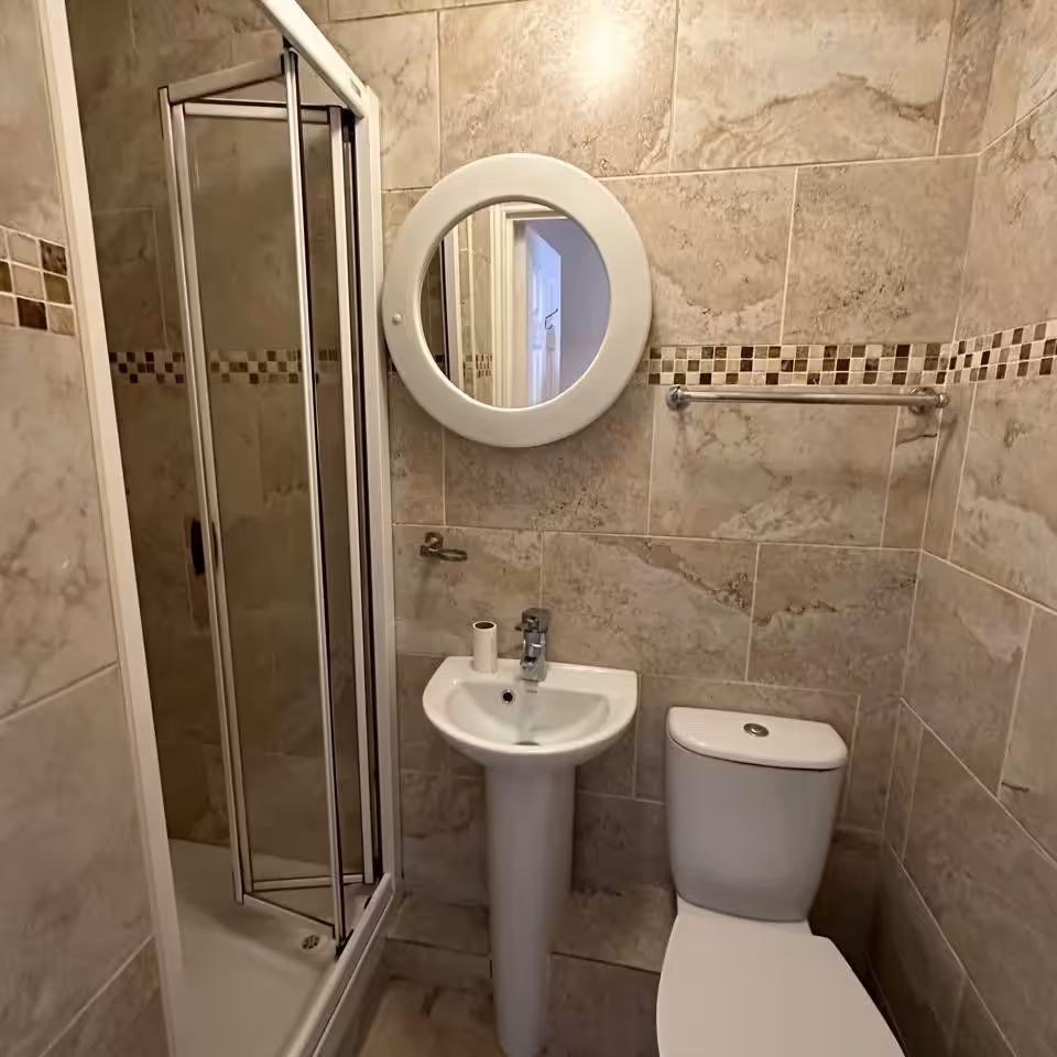 Small bathroom with shower, toilet, sink, mirror, and tile walls.