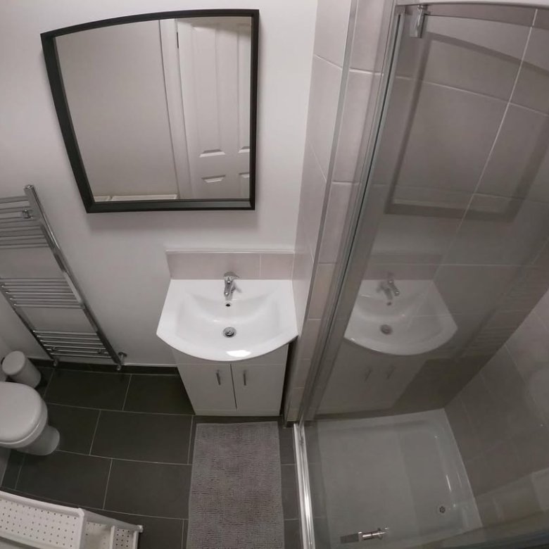 Small bathroom with shower, toilet, sink, and mirror. Gray and white color scheme.