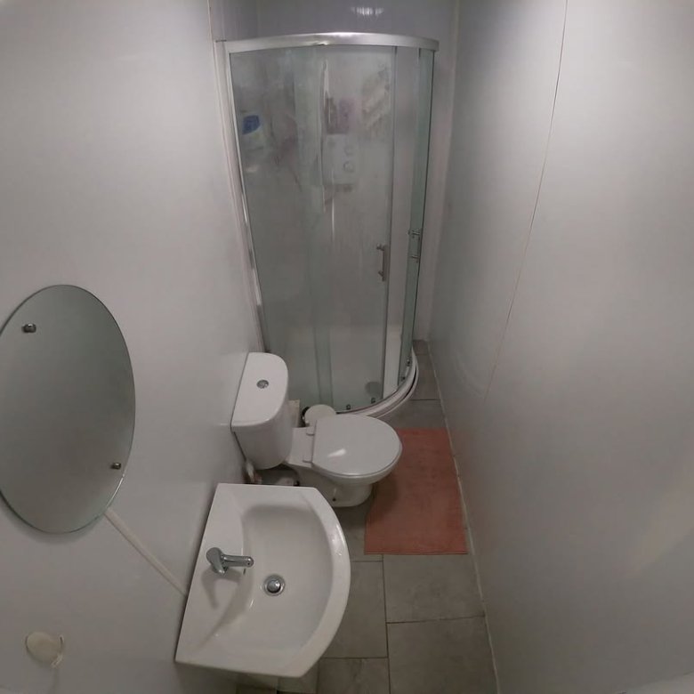 Small bathroom with shower, toilet, sink, and round mirror on a white wall.