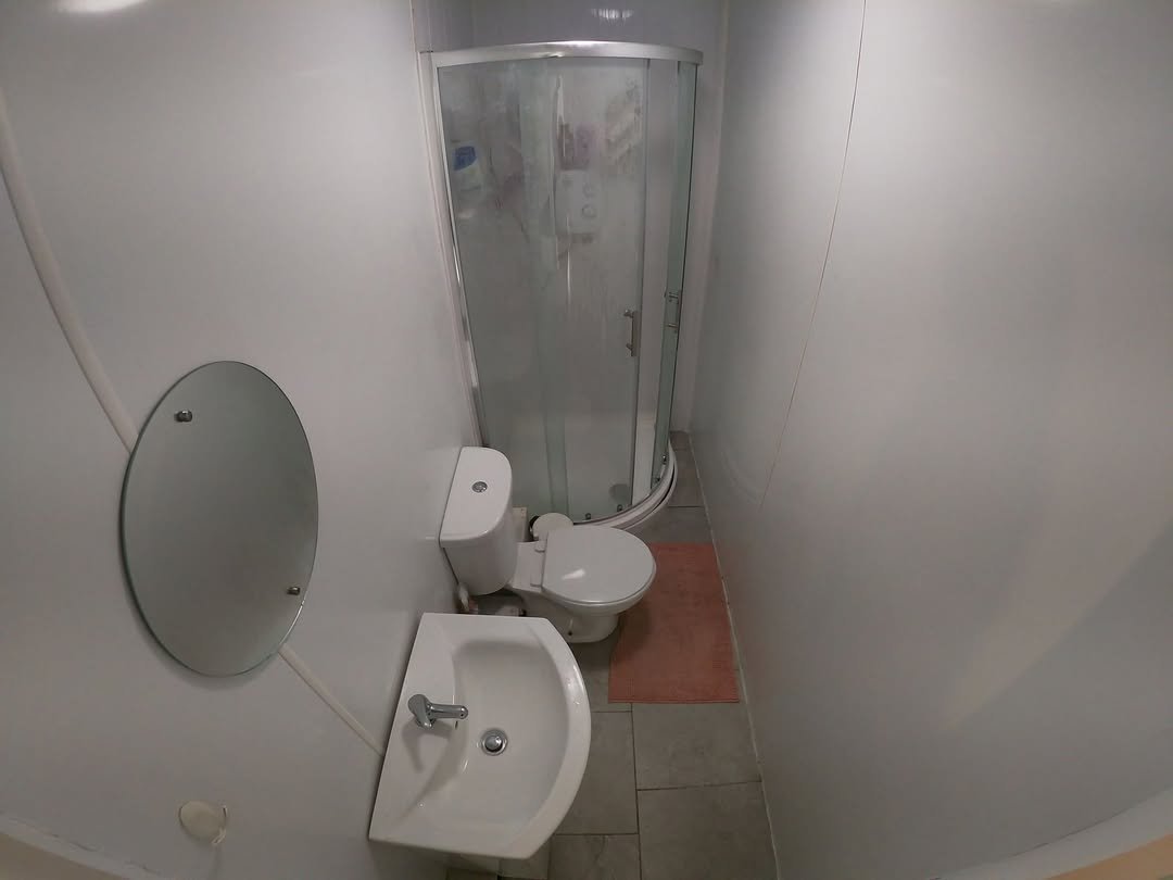 Small bathroom with shower, toilet, sink, and round mirror on a white wall.