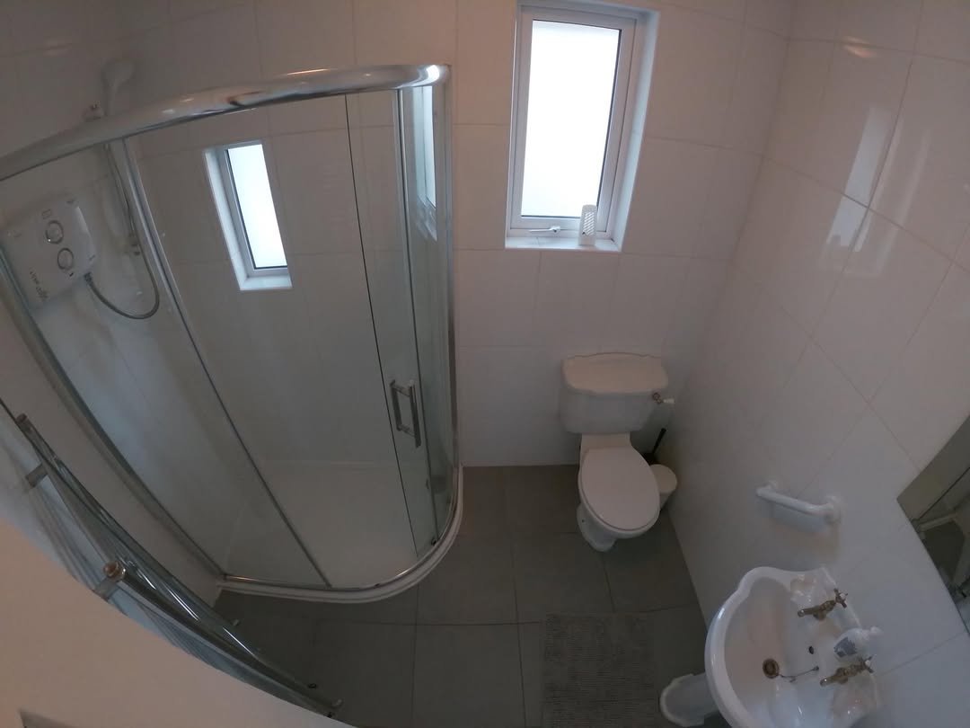 Small bathroom with shower, toilet, and sink in a white tiled room.