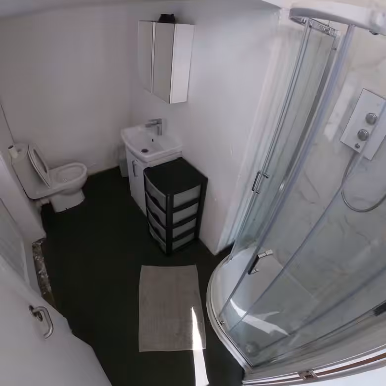 Small bathroom with shower, toilet, sink, storage cabinet, and dark floor. White walls and fixtures.