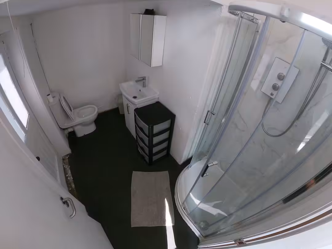 Small bathroom with shower, toilet, sink, storage cabinet, and dark floor. White walls and fixtures.
