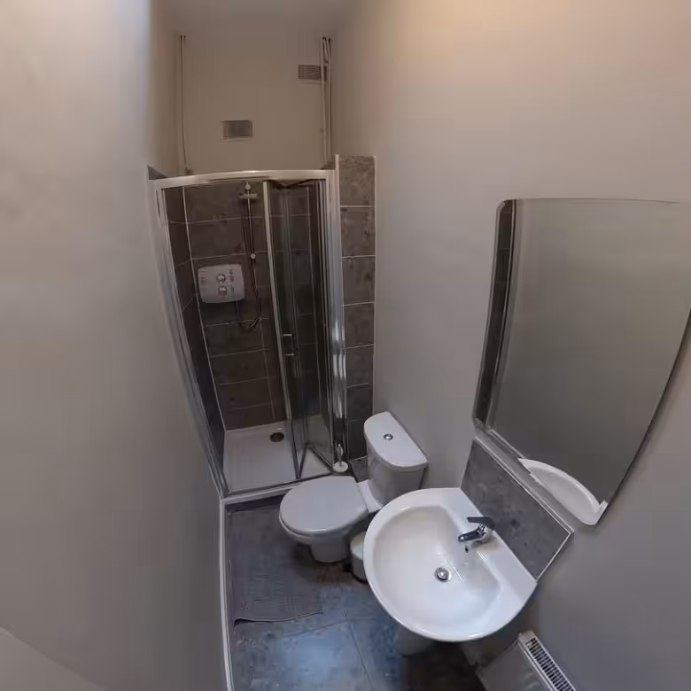 Small bathroom with shower, toilet, sink, and mirror. Gray walls and floor.