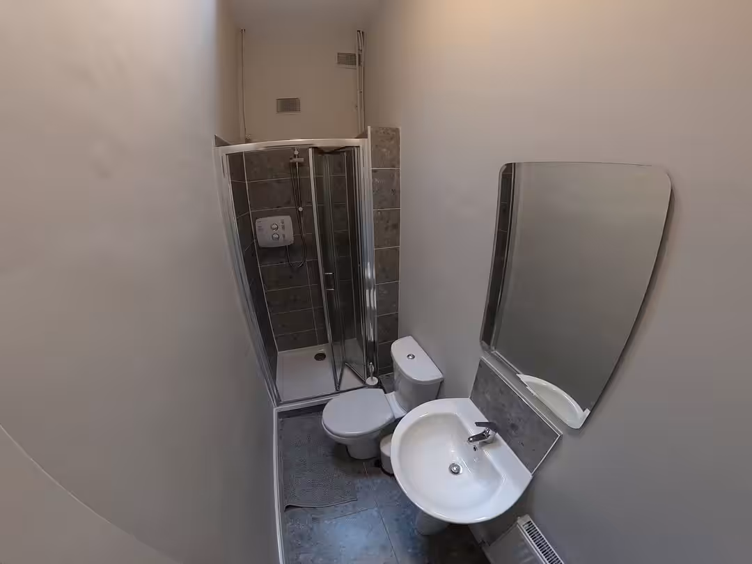 Small bathroom with shower, toilet, sink, and mirror. Gray walls and floor.