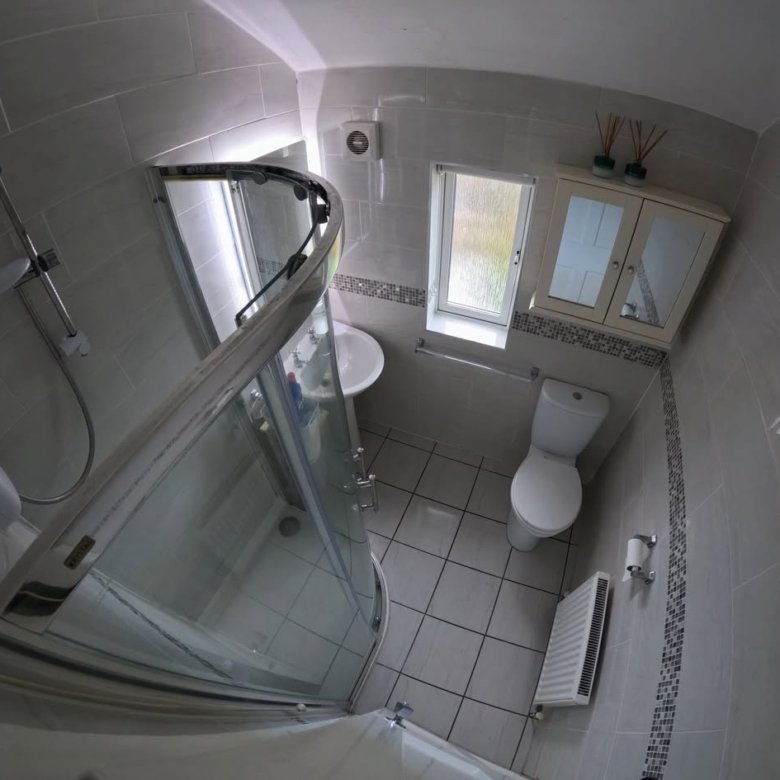 Small bathroom with shower, toilet, sink, and cabinet. Gray tile walls.