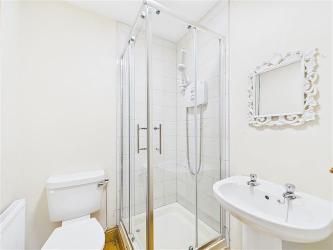 Small bathroom with shower, toilet, sink, and ornate mirror. Neutral color scheme.