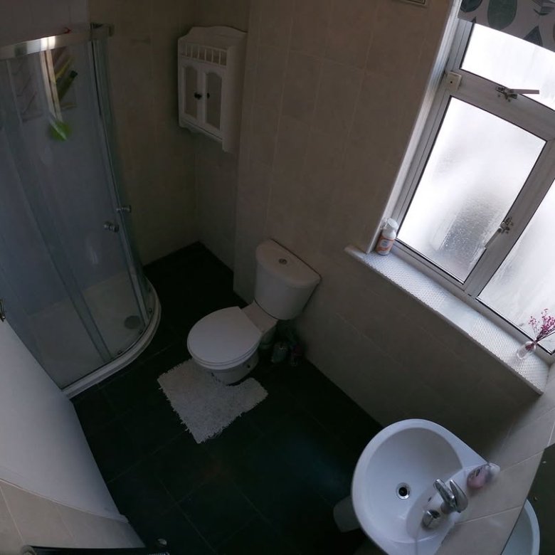 Small bathroom with shower, toilet, sink, and window with patterned curtain.