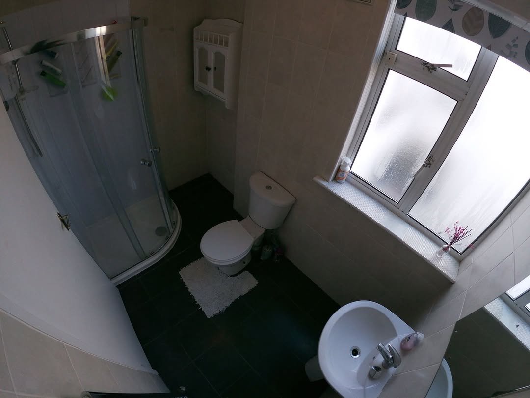 Small bathroom with shower, toilet, sink, and window with patterned curtain.