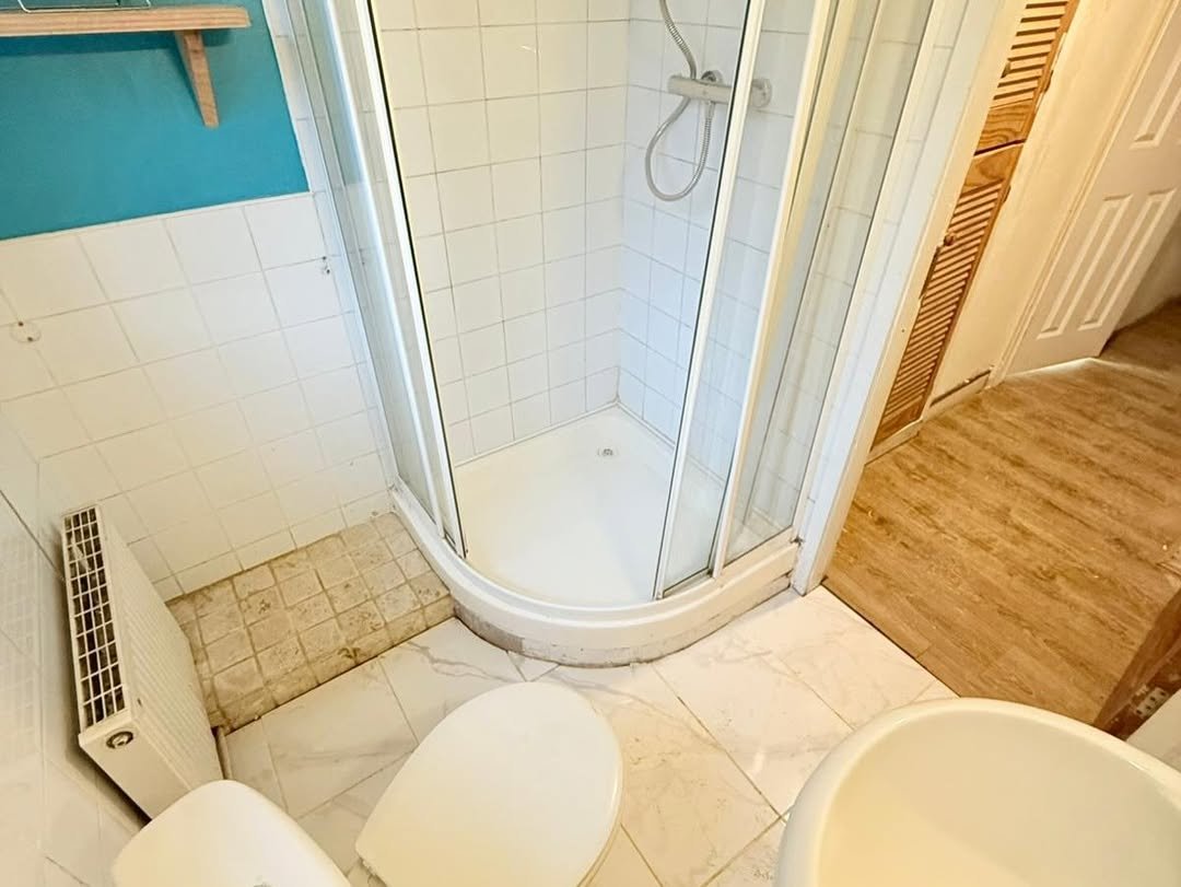 Small bathroom with shower, toilet, sink, and tiling.