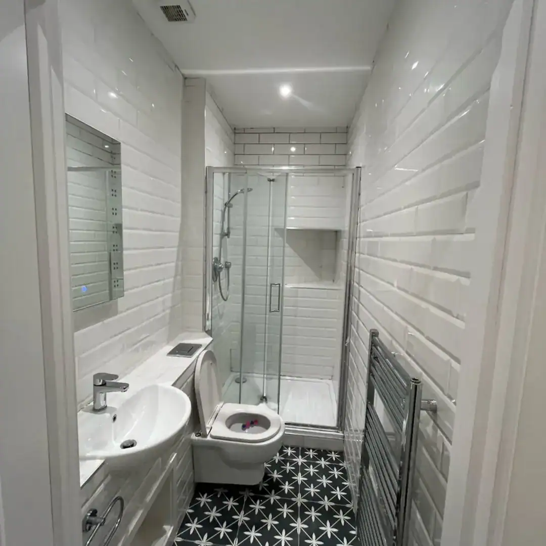 Small bathroom with shower, toilet, sink, and black and white star patterned floor.