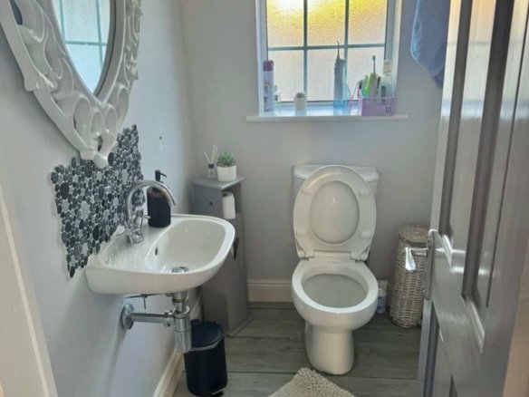 Small bathroom with toilet, sink, heart-shaped mirror, gray walls, and wood-look floors.