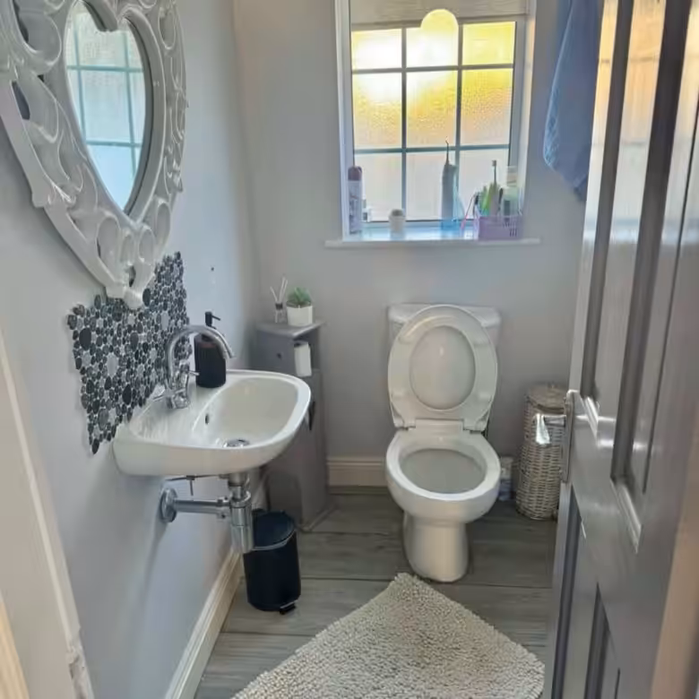 Small bathroom with toilet, sink, heart-shaped mirror, gray walls, and wood-look floors.
