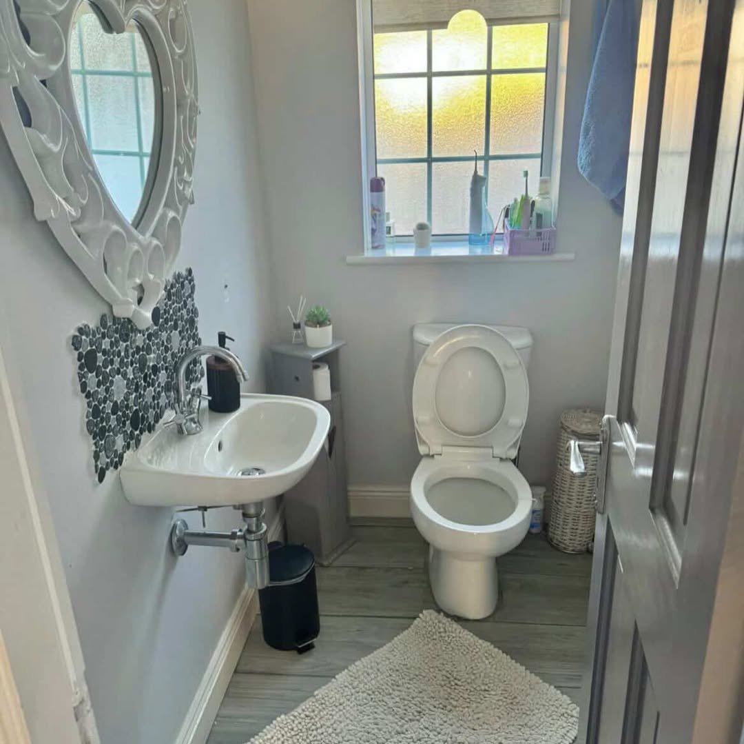 Small bathroom with toilet, sink, heart-shaped mirror, gray walls, and wood-look floors.