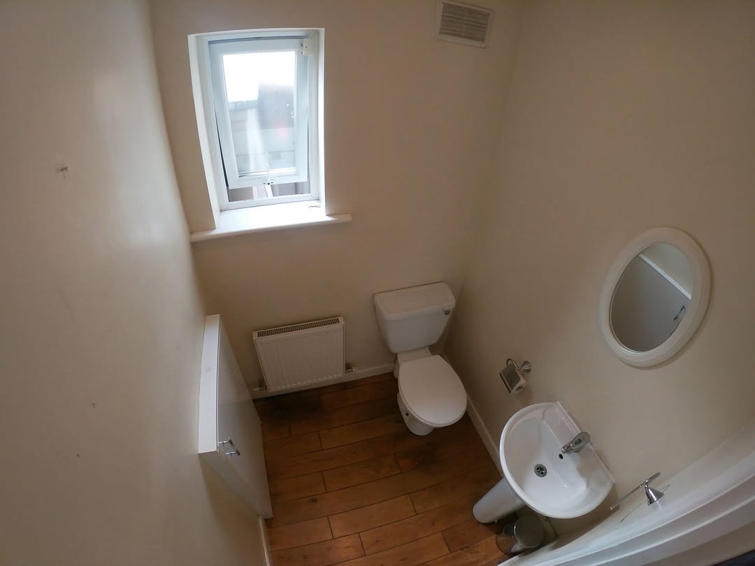 Small bathroom with toilet, sink, mirror, radiator, and window.